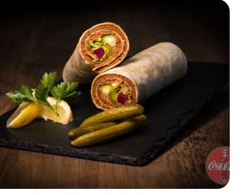 Aufgeschnittener Çiğköfte Dürüm auf einer Schieferplatte mit Gewürzgurken und Zitrone.