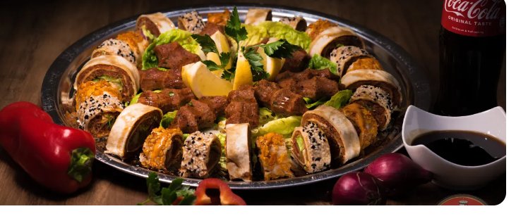 Große Servierplatte mit Çiğköfte Sushi, Wraps, frischem Gemüse und Dips.